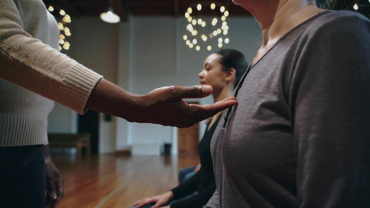 Guiding facilitator extending open hand toward seated woman in gray top in studio