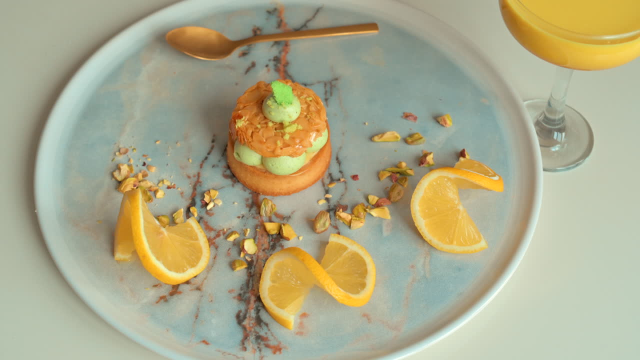 Primer plano de un postre de pistacho con rodajas de limón en un plato cerca de un vaso de zumo de naranja