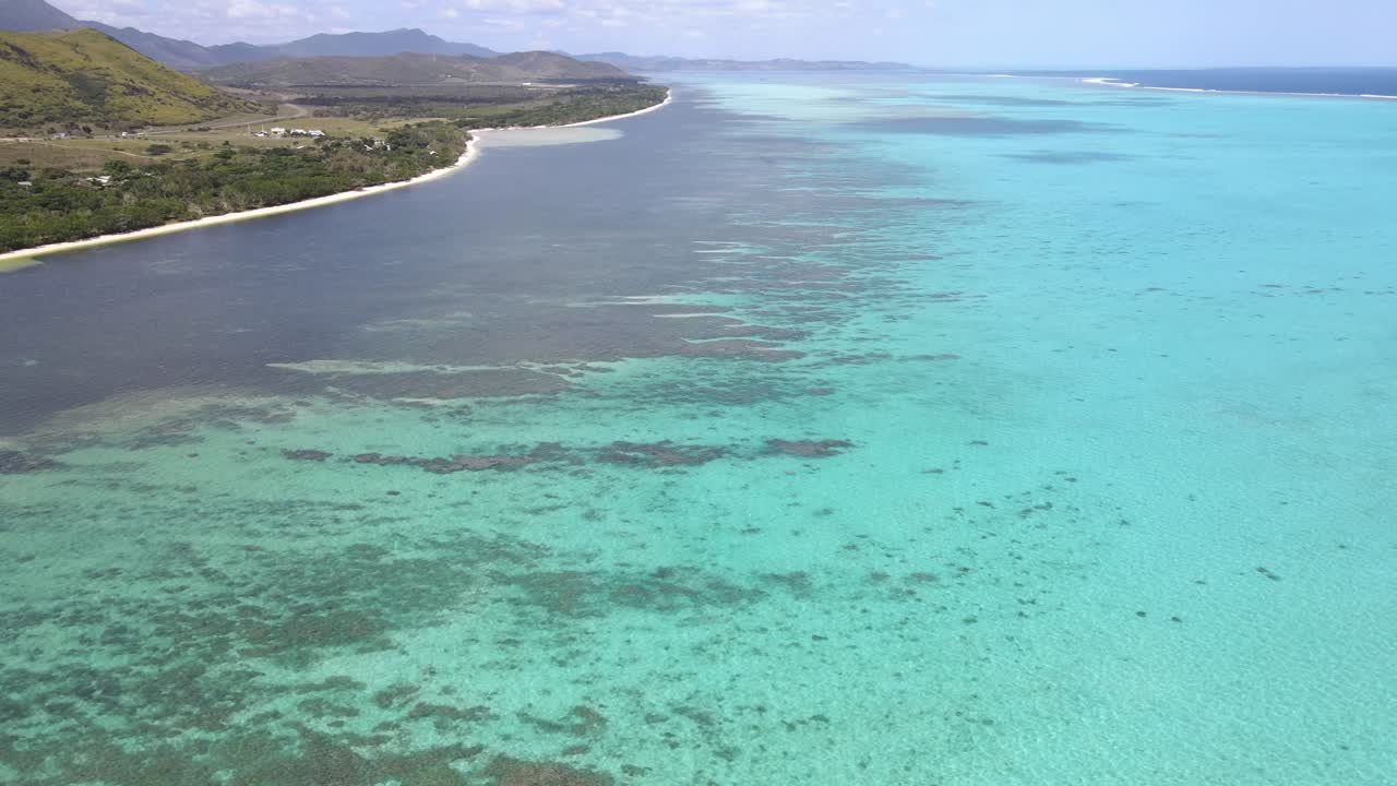 Drone aerial moving down and panning over a blue ocean and showing a mountainscape in New Caledonia