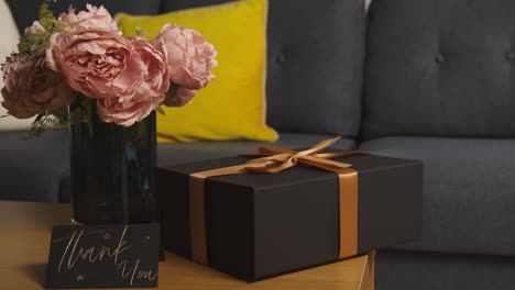 close up of gift wrapped present with thank you card and flowers on table in lounge at home