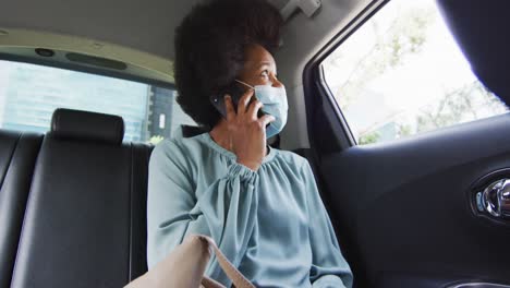 mujer de negocios afroamericana con máscara facial hablando en un teléfono inteligente