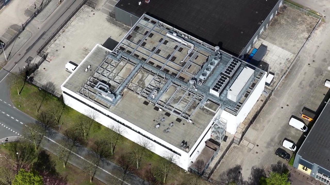 High angle drone footage showing the rooftop of a large, modern data center building, featuring extensive hvac systems, air conditioning units, and ventilation ductwork for cooling