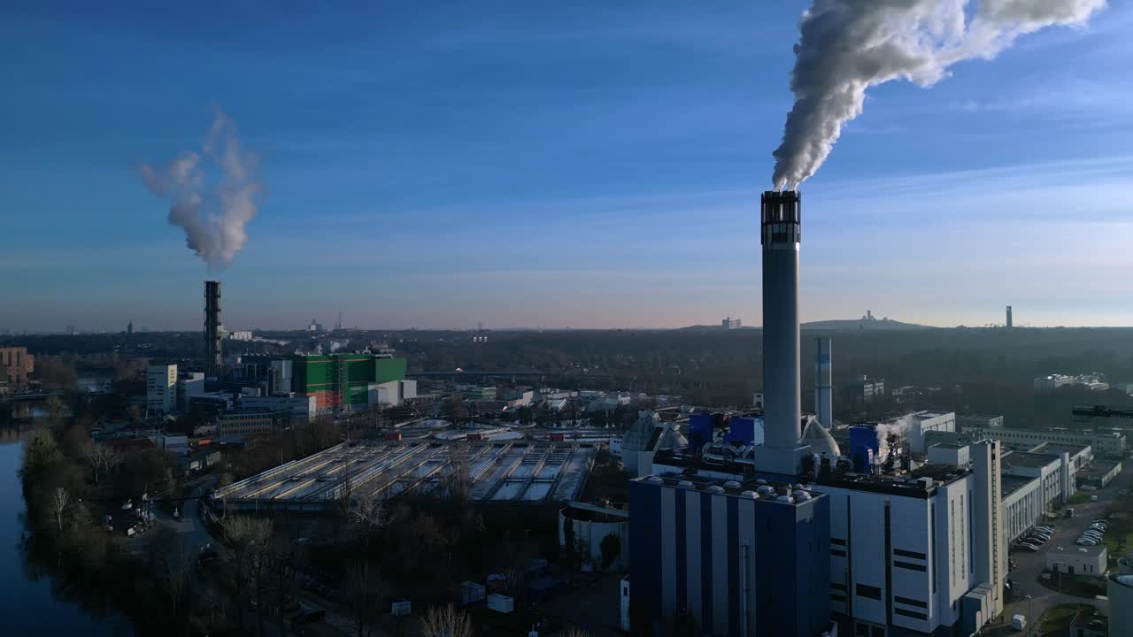 Impianto di termovalorizzazione dei rifiuti urbani con grandi ciminiere che emettono vapore in un cielo azzurro, che illustra lo sviluppo urbano sostenibile. Migliore vista aerea panoramica, statica, da drone con treppiede sospeso