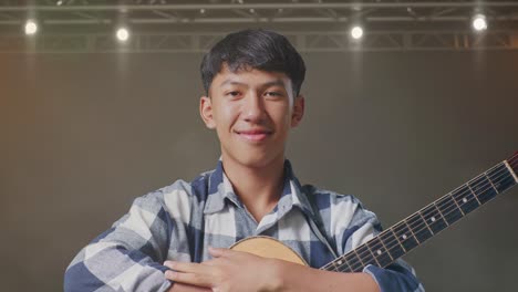 primer plano de un adolescente asiático con una guitarra cruzando los brazos y sonriendo en el escenario