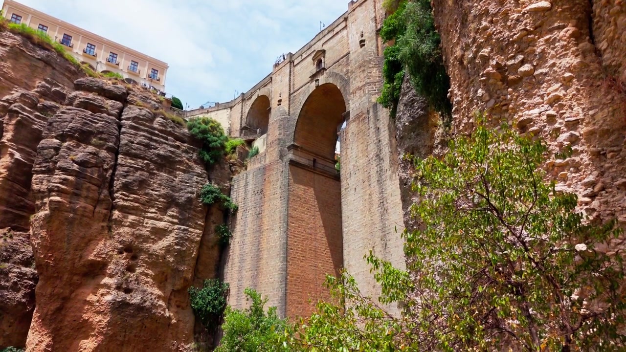 Panoramica dal basso verso l'alto e viceversa sotto il famoso Puente Nuevo di Ronda, che rivela la spettacolare gola di El Tajo, le scogliere rocciose e la vegetazione rigogliosa sottostante