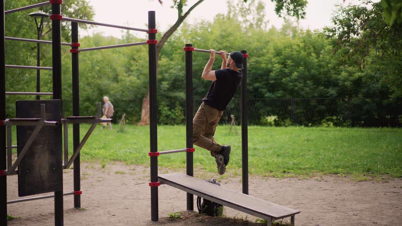 Park PullUp Training By White Man, Strict Vertical Pulls On Metal Bar, Knuckles Gripping, Lats And Shoulders Engaged, Summer Greenery Backdrop, Focused Repetition And UpperBody Strength Focus