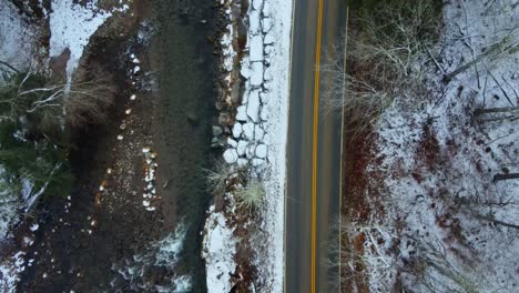 Ariel-view-of-a-snowy-forest-and-stream-running-alongside-a-mountain-in-early-December