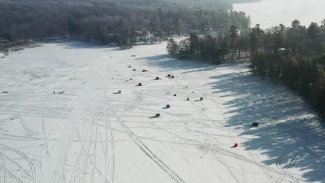 Aerial,-ice-fishing-houses-on-a-frozen-lake-during-the-winter-day