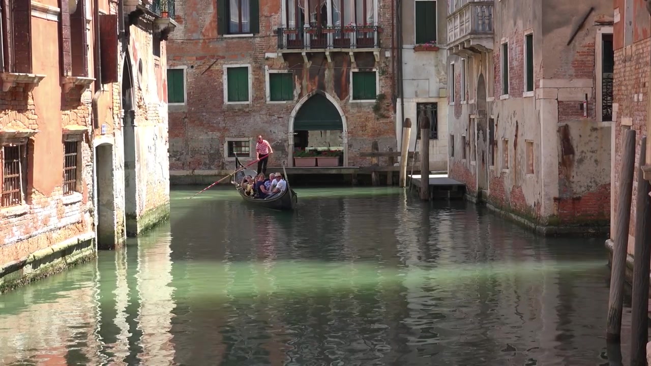 Gondolero navegando con turistas por un estrecho canal de Venecia