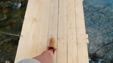 a man in trekking boots walks along the edge of a wooden bridge over the precipice pov video