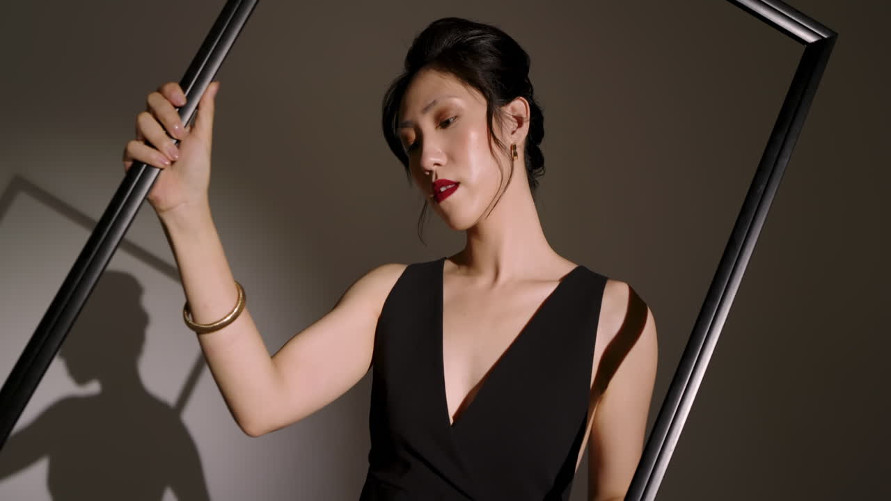 Asian Chinese female model lifting and tilting black frame in studio, casting crisp shadow