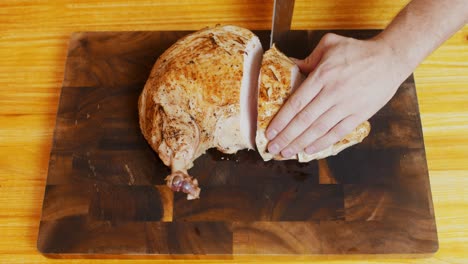 top view of chef cutting freshly grilled turkey meat on wooden cut board