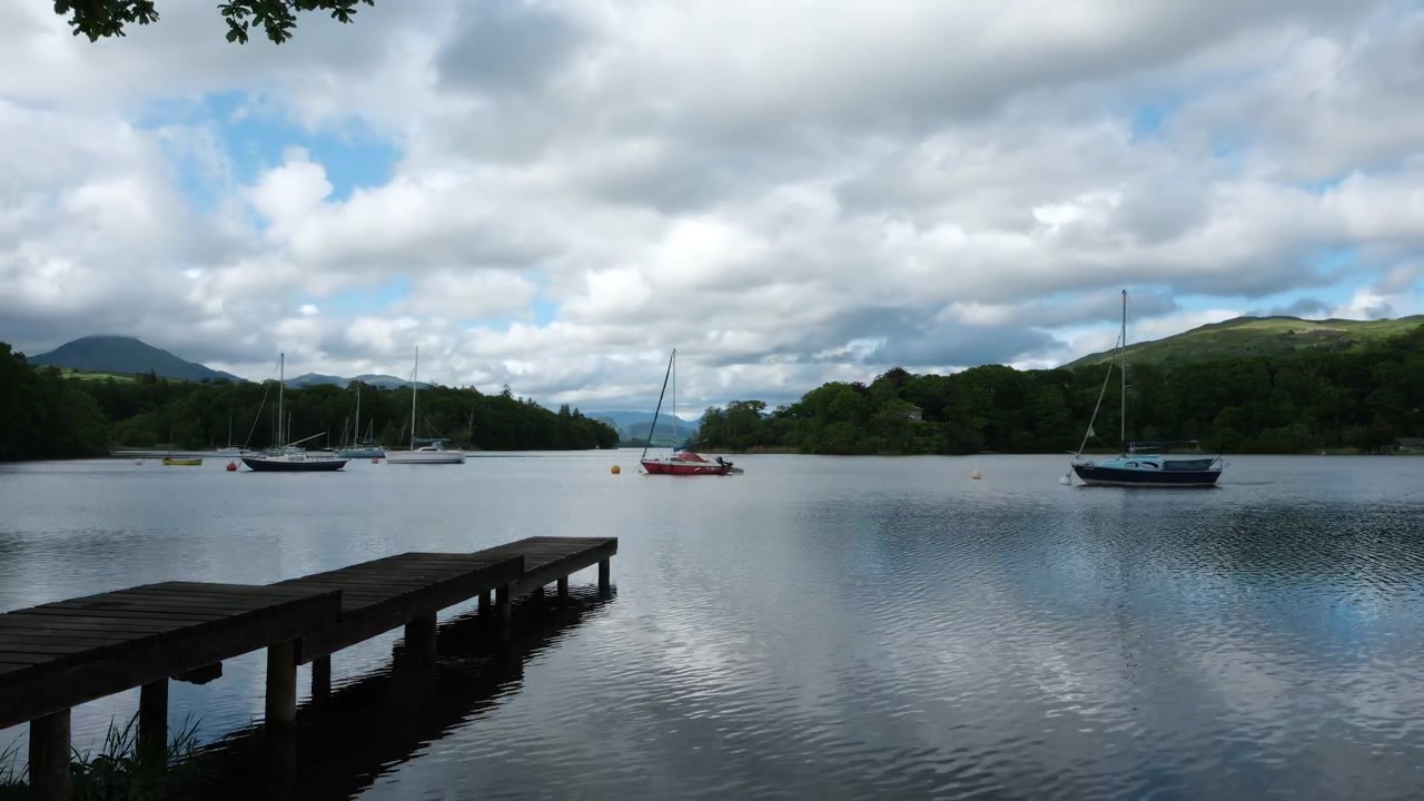 Timelapse overlooking Coniston Water in the Lake District, with sailing boats resting on calm water beneath fast-moving clouds and changing light conditions