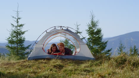 couple lying in tent during hike looking at notebook