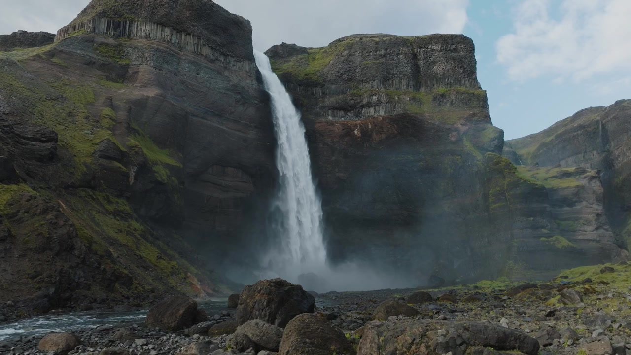 50fps luftfoto av Haifoss, Islands majestetiske foss. Fallende vann stuper ned i en steinete kløft omgitt av mosegrodde klipper og ulendt terreng. Perfekt for natur, reise og landskap