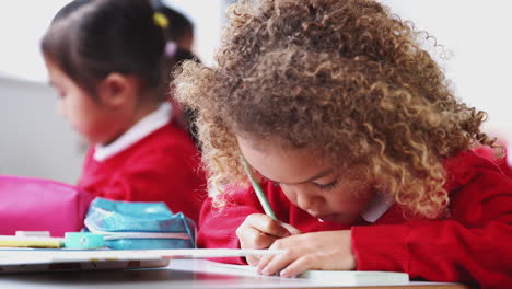 Young-schoolgirl-wearing-school-uniform-sitting-at-desk-in-an-infant-school-class-drawing,-close-up