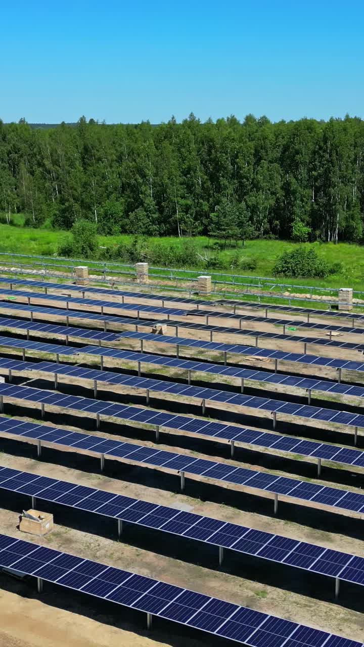 Drone flies vertically over an incomplete solar park site bordered by dense green forest.