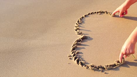 Mädchen-Zeichnet-Ein-Herz-Mit-Den-Fingern-In-Den-Sand