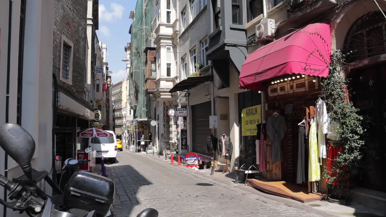 View of a narrow street in Istanbul, Turkey, lined with multi-story buildings, with shops and vendors on the ground floor, capturing the charm and commerce of the city’s urban fabric.