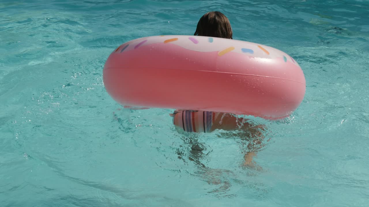 beautiful young girl playing with her inflatable donnuts in the swimming pool