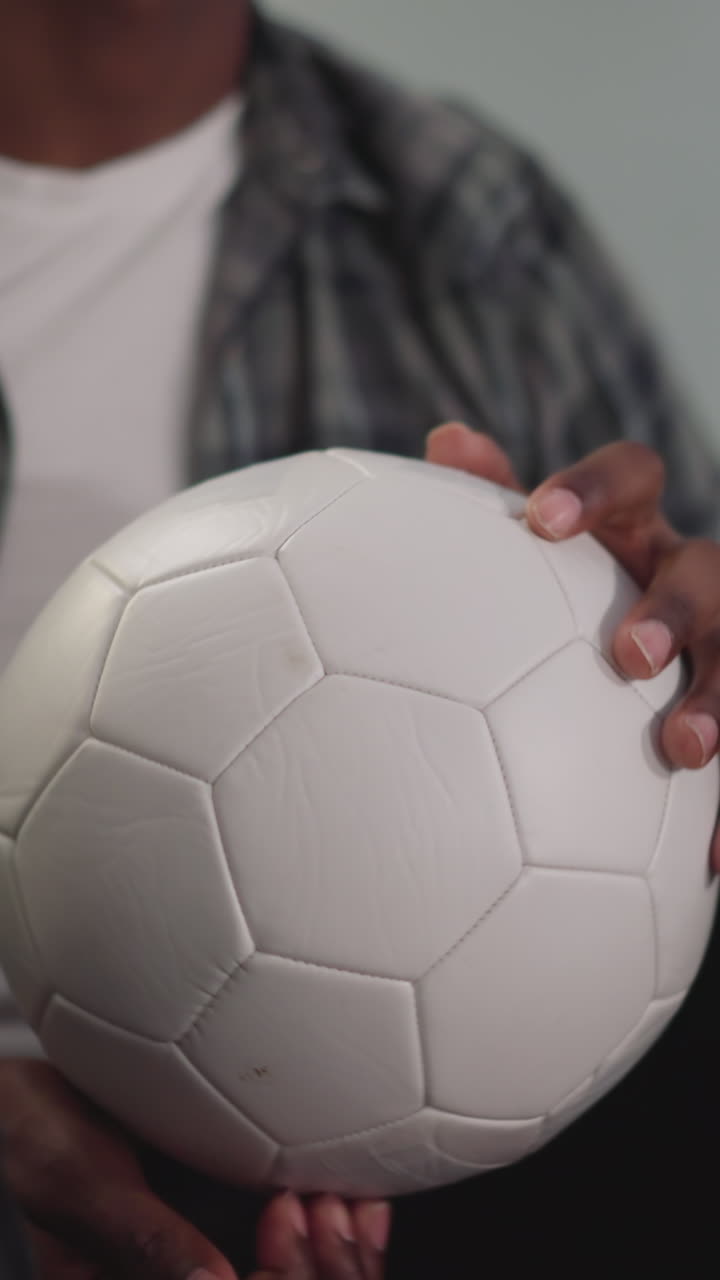 joven afroamericano juega con una pelota blanca sentado en una silla de frijol en close-up en cámara lenta. jugador de fútbol descansa en casa. deporte y estilo de vida activo