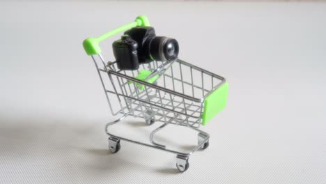 toy camera in miniature shopping cart of green color on a white or light gray background