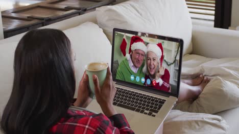 Mixed-race-woman-on-laptop-video-chat-having-coffee-during-christmas-at-home