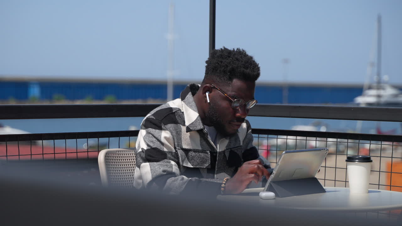 hombre trabajando en una tableta al aire libre en una cafetería.