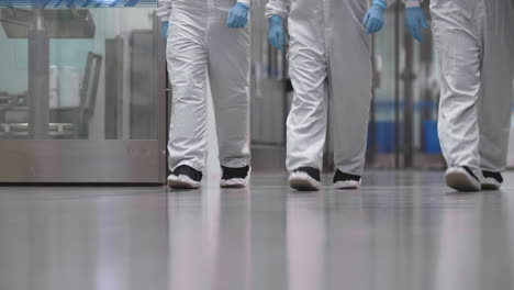 three scientists dressed in full protective equipment walk towards camera inside a laboratory