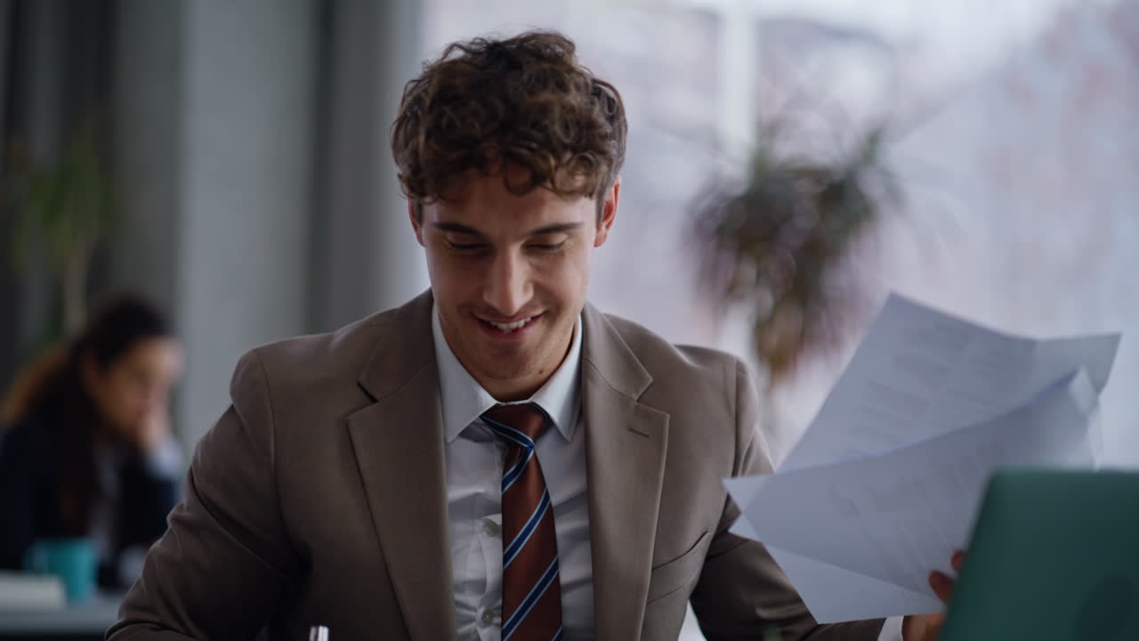 Smiling creator looking papers sitting laptop table workplace in office closeup