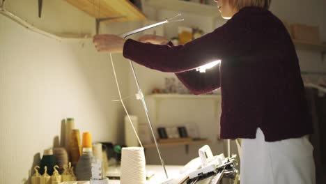 Craft-woman-pulling-thread-in-knitting-machine-standing-on-table-in-workshop