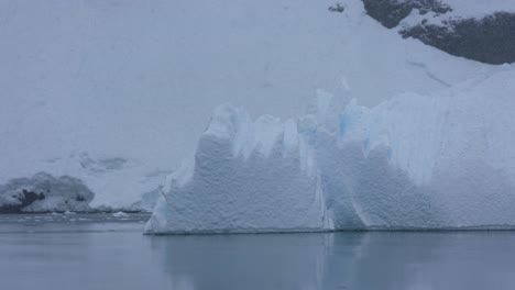 Iceberg-Flowing-by-Snow-Capped-Coast-of-Antarctica-on-Snowy-Day,-Close-Up