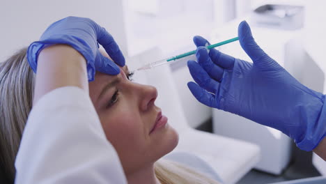 woman sitting in chair being give botox injection between eyes by female doctor