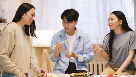 tres amigos japoneses sentados alrededor del mostrador de la cocina cortando y comiendo sushi 2