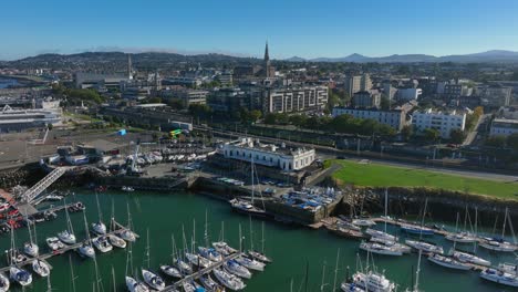 royal irish yacht club, dún laoghaire, county dublin, ireland, september 2024. drone clockwise orbit pulls back to reveal sailboats lining the marina under a beautiful blue sky.