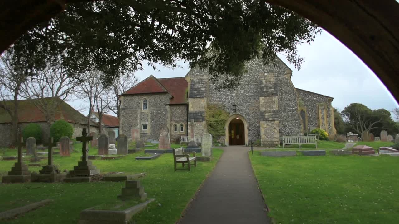 lychgate의 아치를 통해 st margaret's church, rottingdean, east sussex의 교회 마당을 바라보고 있습니다.