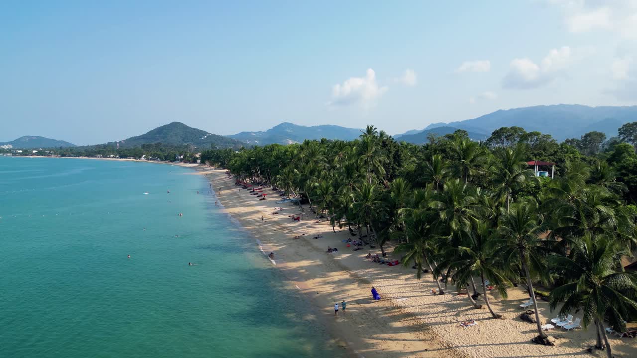 Aerial footage of Mae Nam Beach, Koh Samui, Thailand, showcasing turquoise waters, sandy shores, and lush palm trees under a clear sky