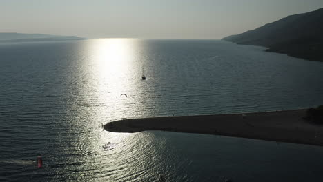aerial view of silhouetted kite surfers at sunset next to sand peninsula, zlatni rat, croatia
