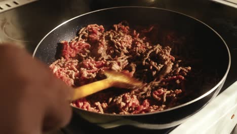 person cooking ground meat in a pan on a stove, stirring it with a spatula