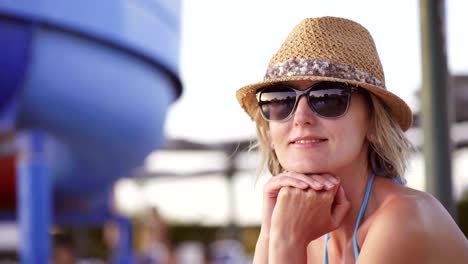 woman in swimwear sitting by swimming pool looking at camera smiling