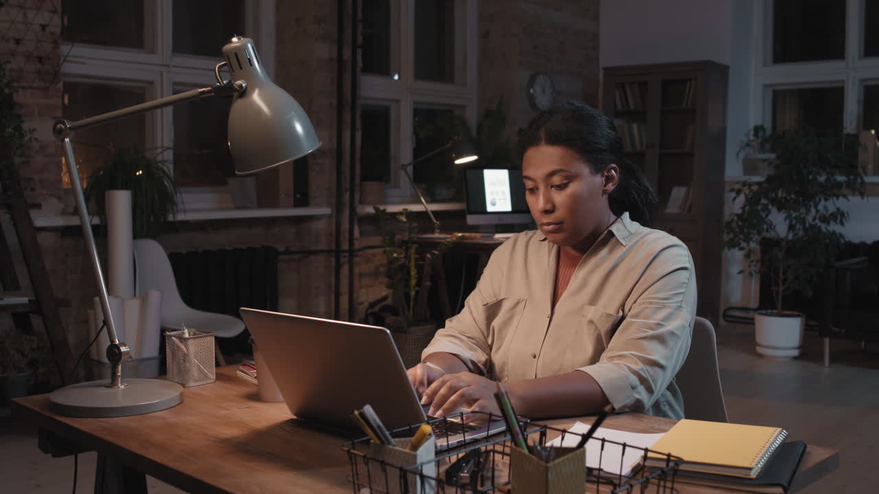 Woman Working on Laptop in Dark Office at Night