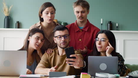 vista frontal del grupo de estudio haciendo un selfie sentado en la mesa con computadoras portátiles y portátiles