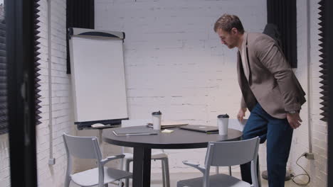 Geschäftsmann-Sitzt-Und-öffnet-Laptop-Computer,-Während-Er-Im-Sitzungssaal-Kaffee-Zum-Mitnehmen-Trinkt