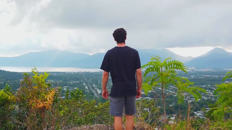 Man approached peaceful lookout of cairns in australia, mountains in the background are covered by clouds and hiding the morning sun