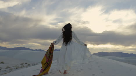 A-woman-skips-across-a-sand-dune-on-a-cloudy-day