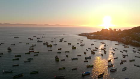 zoom in aerial view of fishing boats stopped with the sunset and the sun in the background, tongoy, chile