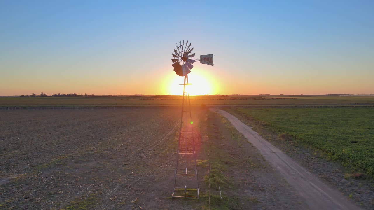 일몰 풍경, 아르헨티나 파타고니아 라 팜파의 경작지 한가운데에서 회전하는 구식 윈드 펌프를 포착한 영화 같은 공중 추적 샷