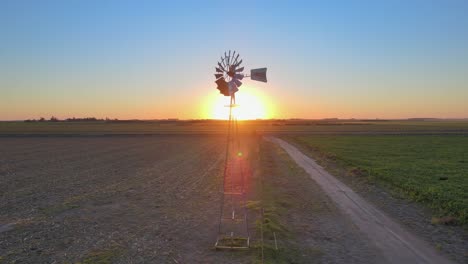 sunset landscape, cinematic aerial tracking shot capturing old fashioned windpump spinning in the middle of arable land in la pampa, patagonia, argentina