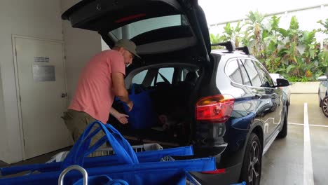 un hombre maduro desempacando un carrito de compras y cargando las compras en la parte trasera de un auto