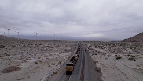 cargo train passing by the desert in palm springs with wind turbines